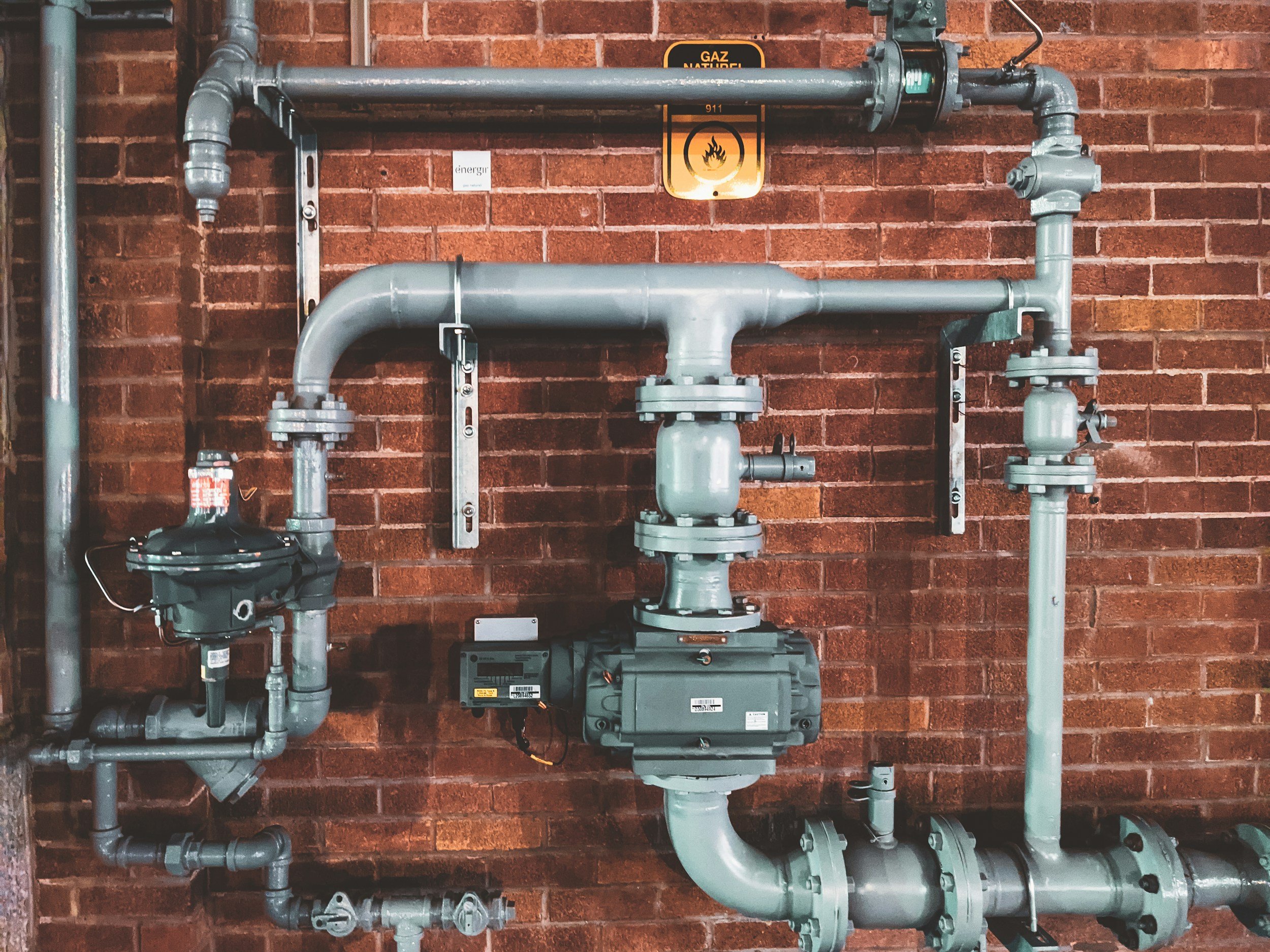 Industrial natural gas piping mounted on a red brick wall